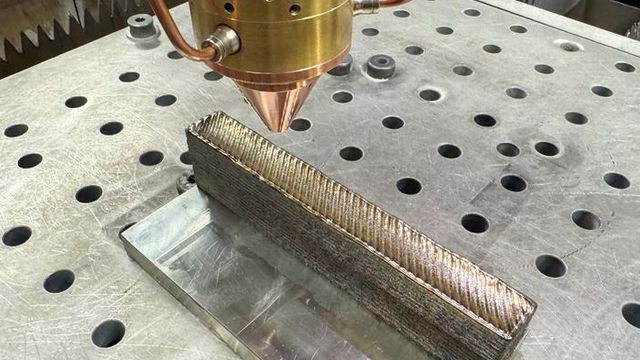 A sample of the new 3D printed titanium. It has a diagonal stripe pattern from the 3D printing nozzle and looks like a rounded metal bar. 