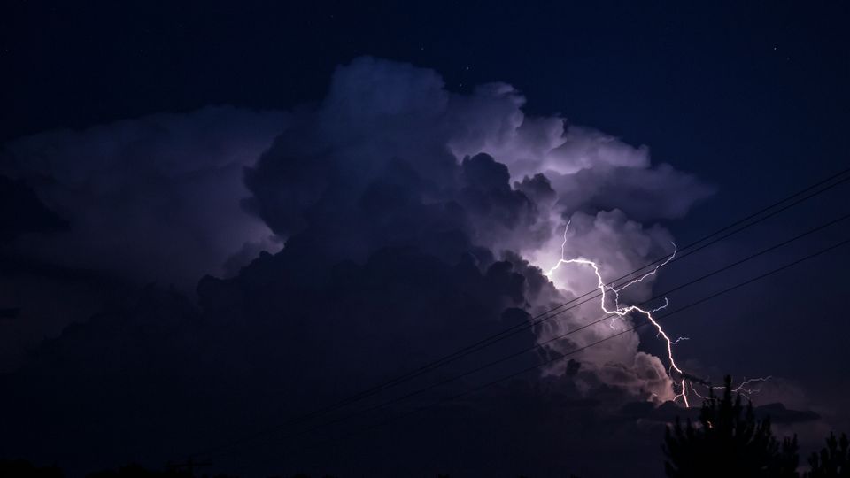 Lightening emerging from clouds at night, power lines visible.