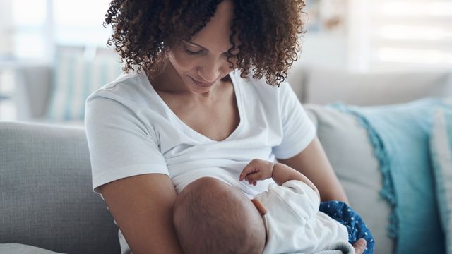 Mother breastfeeding her baby while sitting on a couch in a cozy home setting.