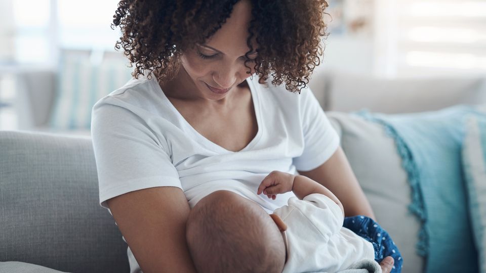 Mother breastfeeding her baby while sitting on a couch in a cozy home setting.