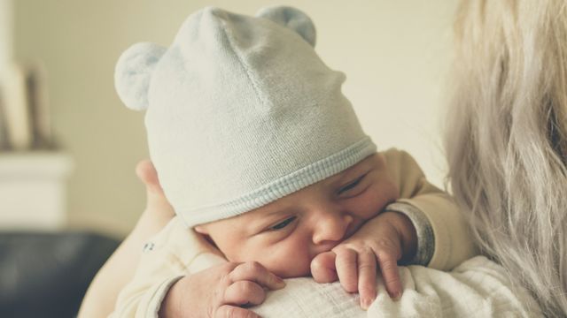 Newborn baby in a blue hat resting on a caregiver’s shoulder, highlighting birth and sex assignment.