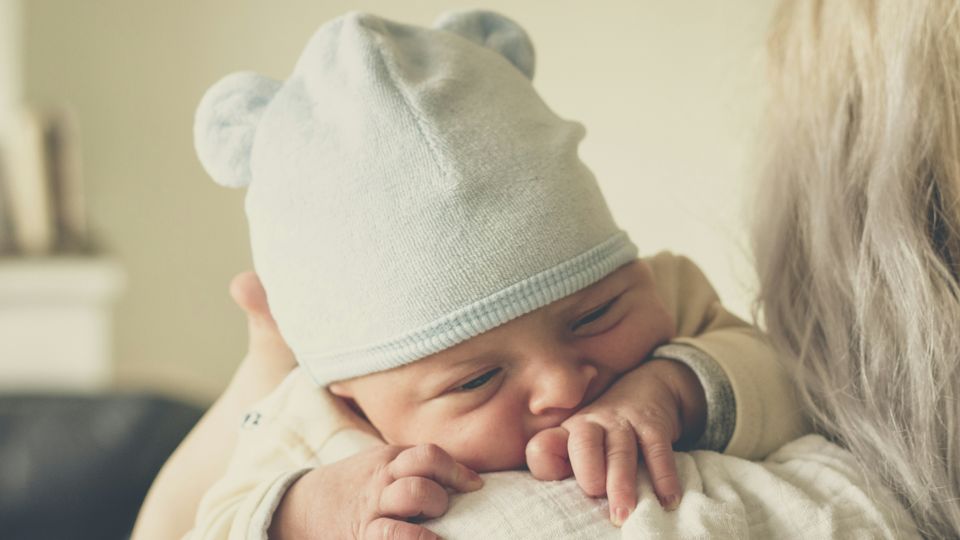 Newborn baby in a blue hat resting on a caregiver’s shoulder, highlighting birth and sex assignment.
