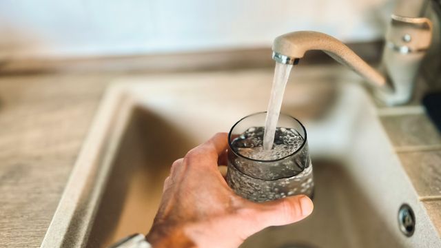 A running tap filling up a glass, held in a person's hand over a sink. 