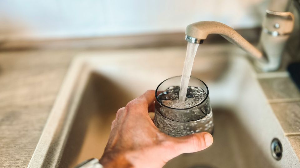 A running tap filling up a glass, held in a person's hand over a sink.