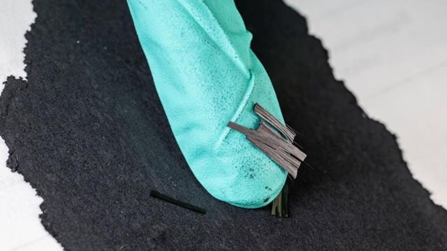 Small lengths of carbon fiber resting on the gloved fingernail of a researcher.