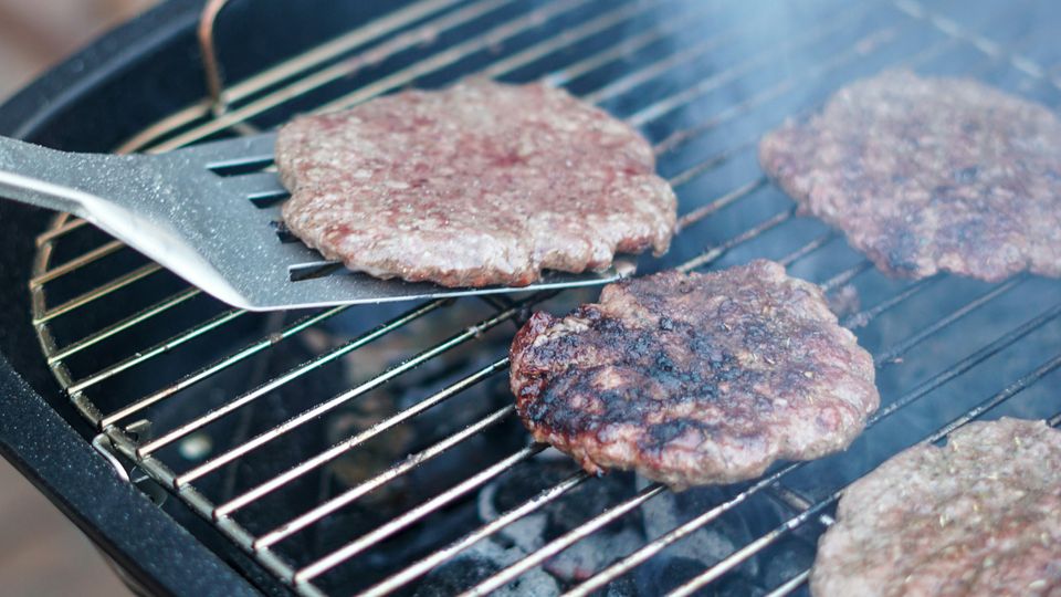 Burger patties on a grill, smoke and spatula visible.