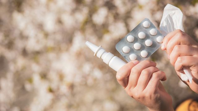 A woman with allergies holding drugs, nasal spray in front of a blooming tree during spring.
