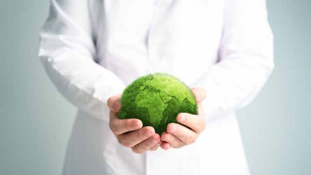 Scientist in white coat holding the Earth that is made from green grass.