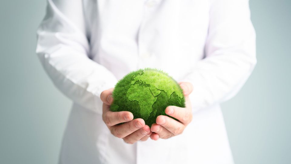 Scientist in white coat holding the Earth that is made from green grass.