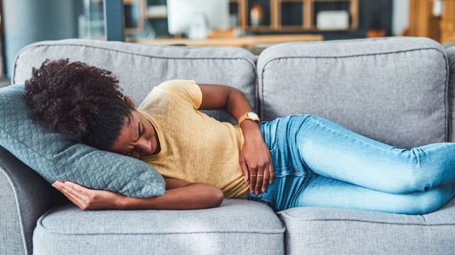 Woman lying down on sofa, clutching stomach, clearly in pain.