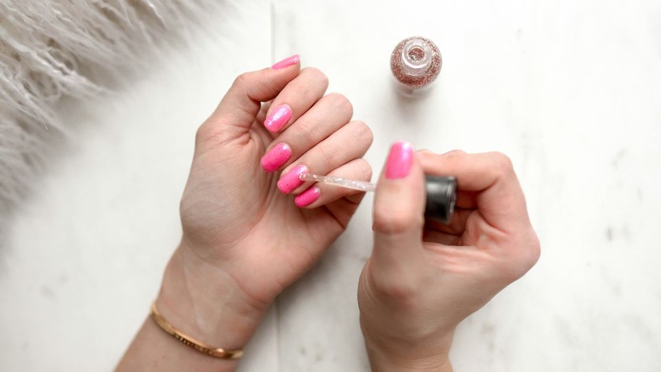 One hand painting the nails of another pink.