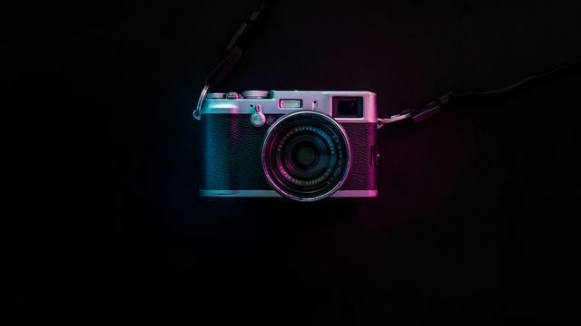 A vintage-style camera on a black background, lit from the sides with blue and red light.