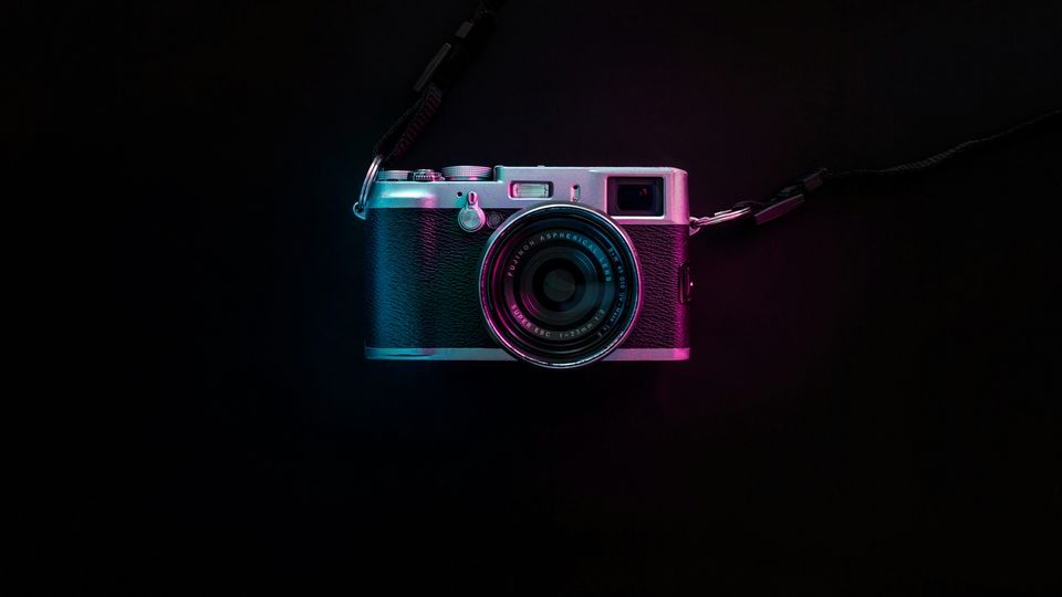 A vintage-style camera on a black background, lit from the sides with blue and red light.