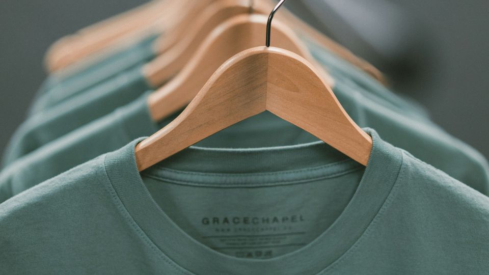 Green jumpers on wooden coat hangers, in a line.
