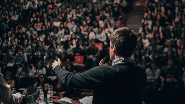 The back of a man giving a speech in front of a lecture theatre.