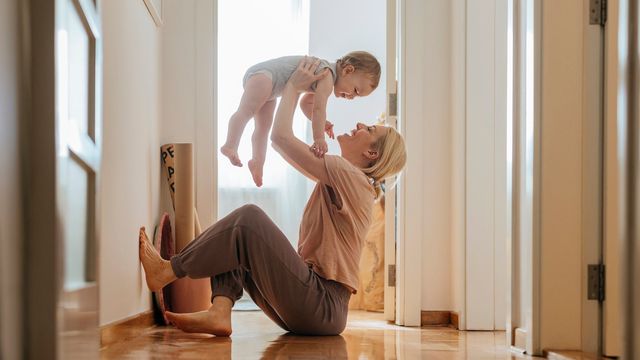 Mother playing with baby in a sunlit hallway, illustrating bonding and early neural development. 