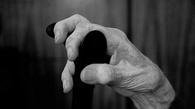 Older persons hand holding a walking stick in greyscale. 