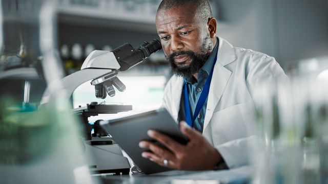 Scientist analyzing data on tablet next to microscope, representing next-generation electron microscopy.