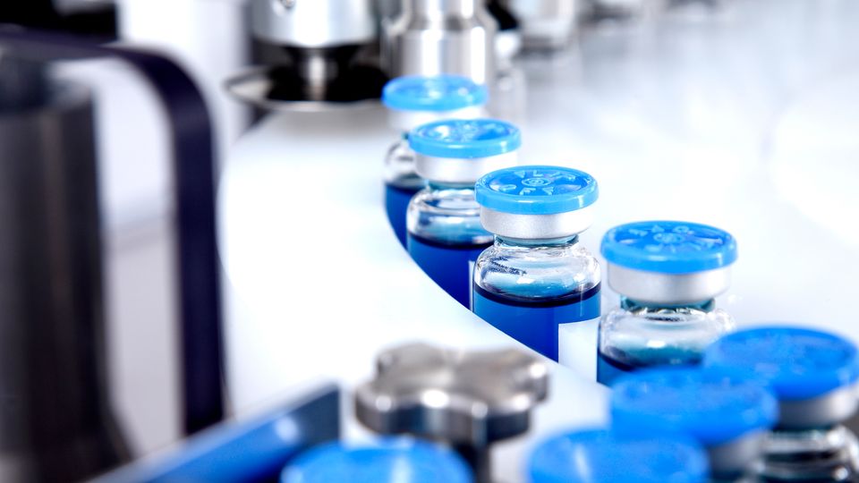  Conveyor belt of vaccine vials  with blue lids.