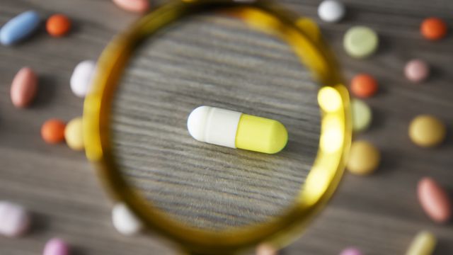 Magnifying glass focusing on a yellow and white capsule, symbolizing drug repurposing research.