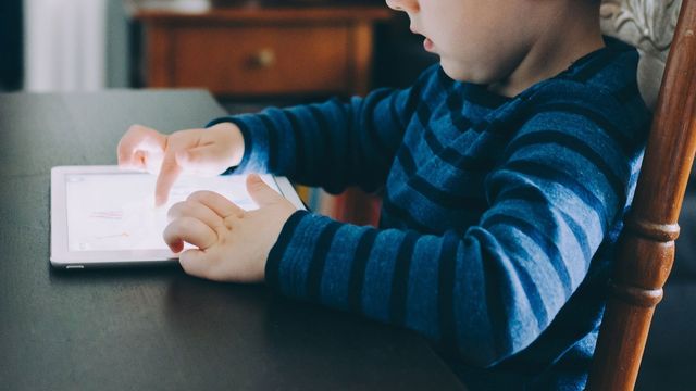 A child in a striped shirt sat at a table using a tablet.
