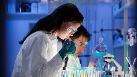 Life science researchers working with lab equipment and liquid samples under blue lighting.