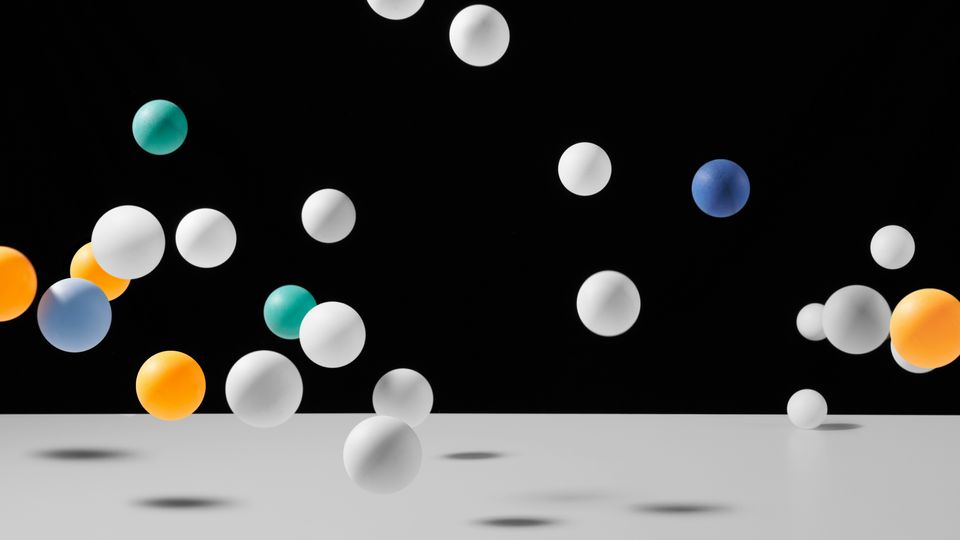 Multicolored bouncy balls bouncing on a white table surface.