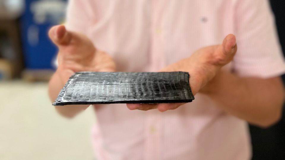 Dr. Mohammad Naraghi holds up a small sheet of ATSP, the carbon-fiber smart plastic. It looks like a small black tablet, roughly the same size as a computer keyboard.