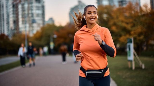 Smiling woman jogging outdoors in an urban park during autumn.