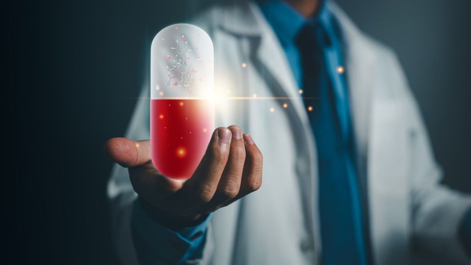 A scientist in a white coat holding up a digitally-imposed image of a red and white drug pill, glowing faintly with data-like lines.