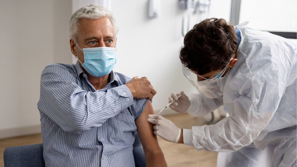 A man wearing a mask receiving a vaccine in his left arm.