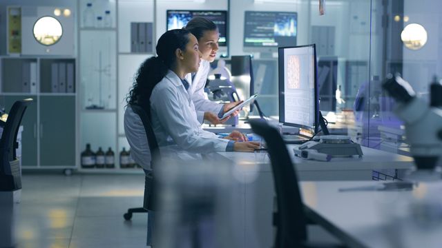 Researchers in lab coats analyzing scientific data on a computer in a modern laboratory.