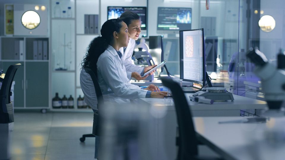 Researchers in lab coats analyzing scientific data on a computer in a modern laboratory.
