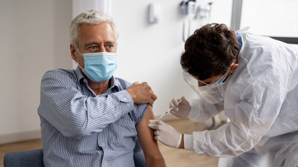 Healthcare worker administering a Chikungunya virus vaccine to an older man wearing a mask.