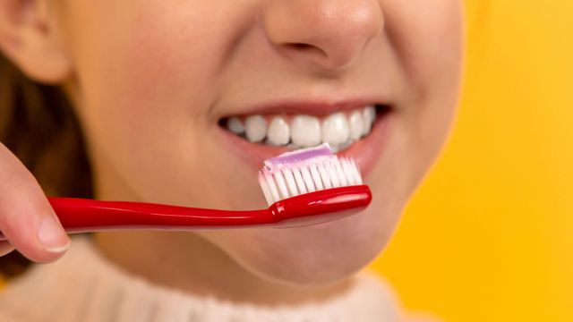 A young girl brushing her teeth with a red toothbrush.