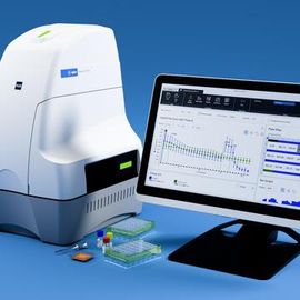Laboratory DNA analysis machine next to a computer monitor displaying scientific data graphs and results. 