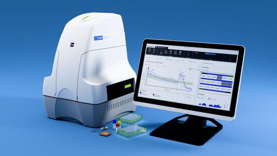 Laboratory DNA analysis machine next to a computer monitor displaying scientific data graphs and results.