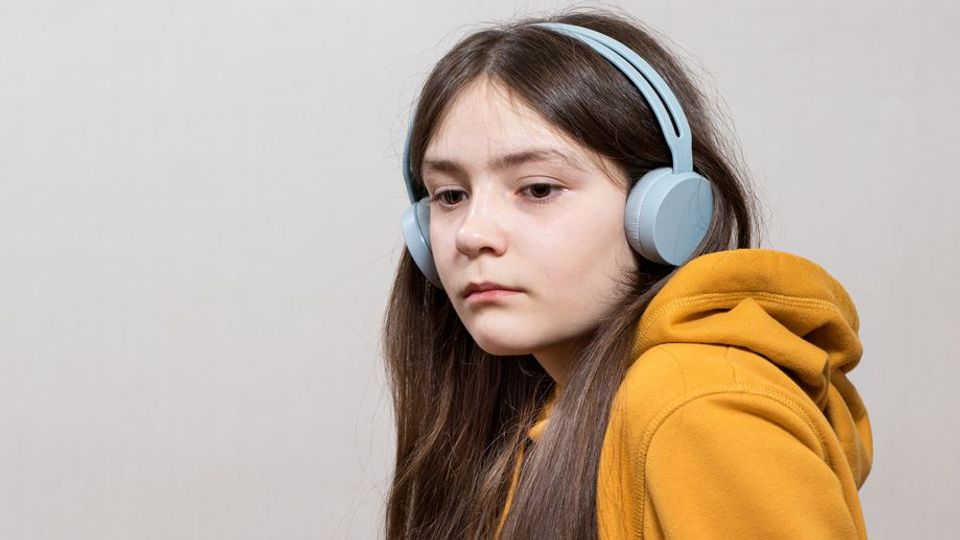 Teen girl wearing headphones and a yellow hoodie, representing autism and ADHD sensory needs.