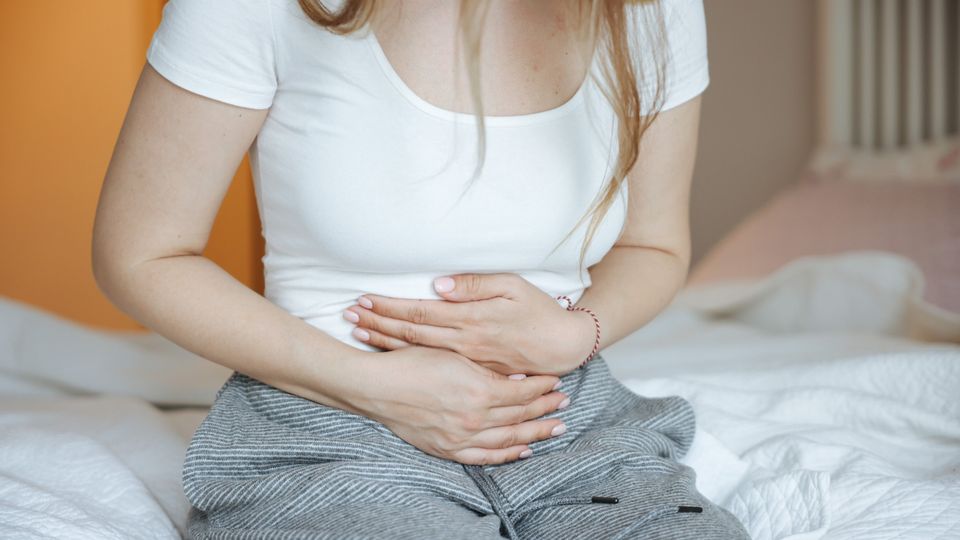 Woman sitting on a bed holding her stomach in discomfort, representing chronic pain.