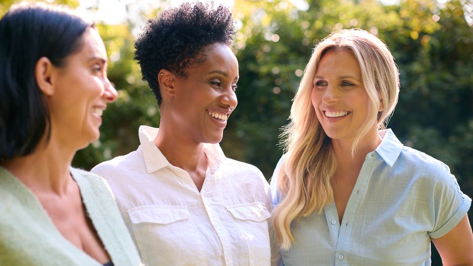 Group of smiling postmenopausal women enjoying conversation outdoors in natural sunlight.