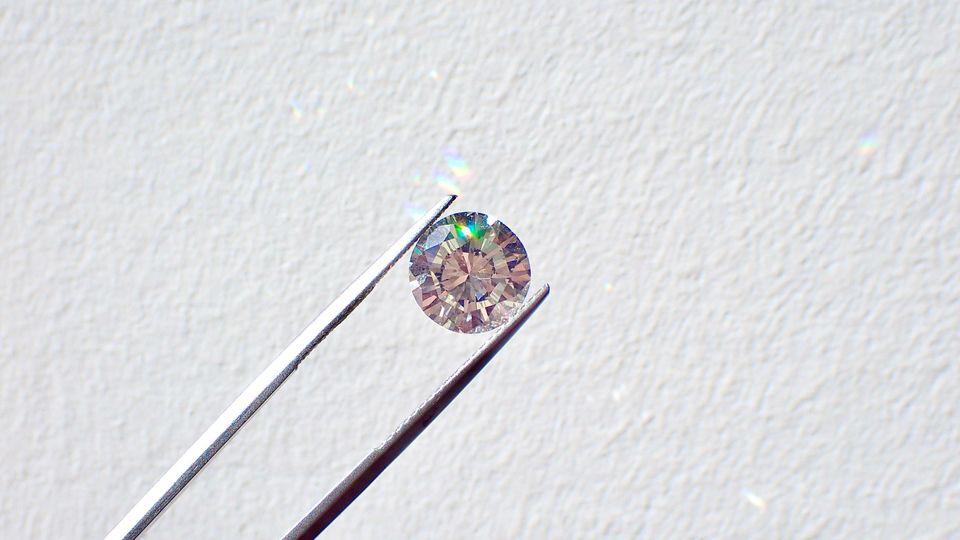A small diamond being held in a pair of long metal tweezers.
