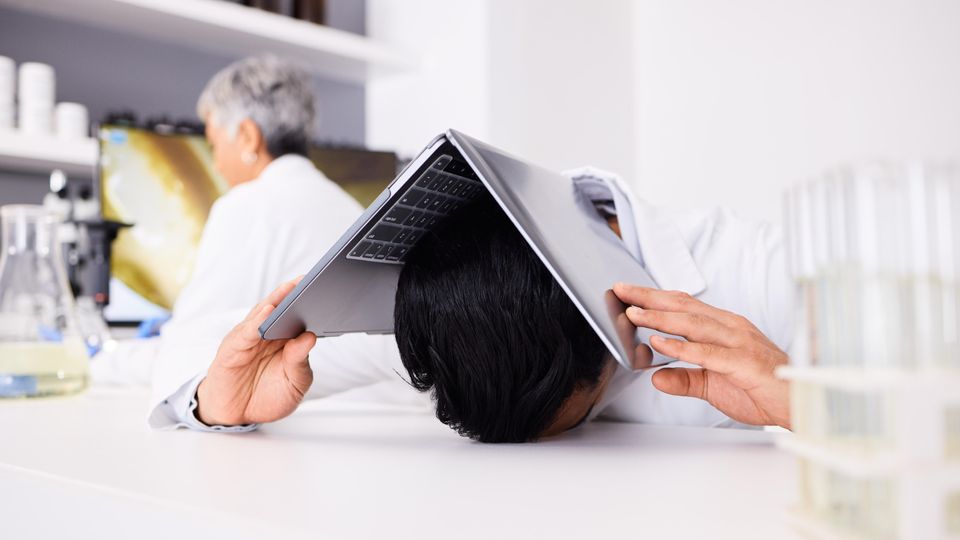 Frustrated scientist holding a laptop over his head in a laboratory.
