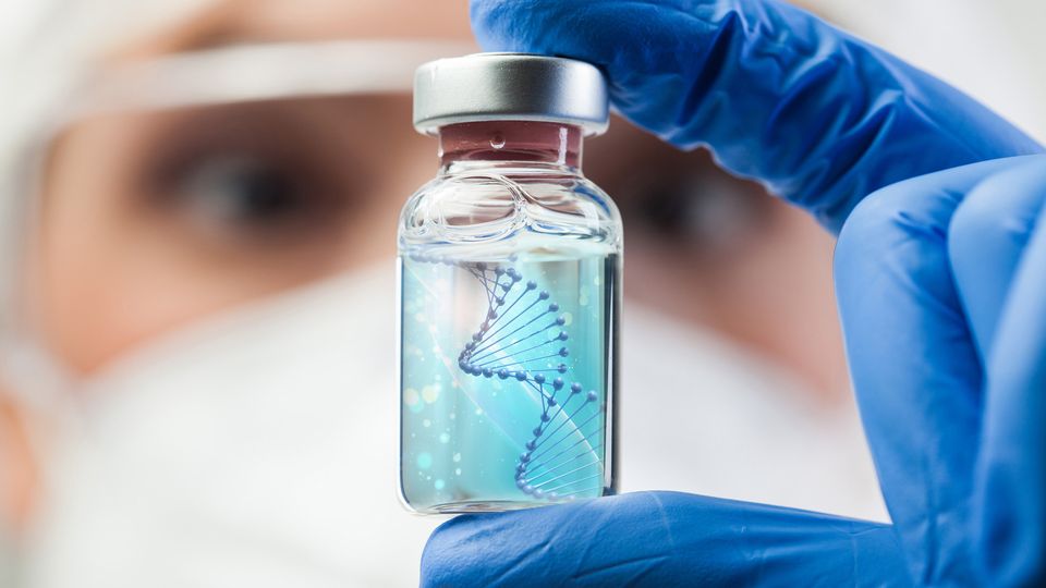 A scientist holding up a vial containing a DNA double helix, representing cell and gene therapy manufacturing.