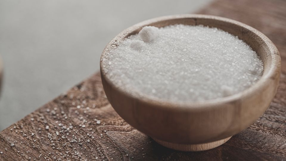 Wooden bowl filled with white granulated salt on a rustic wooden surface.