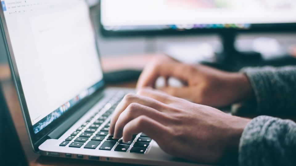 A pair of hands type on a laptop.
