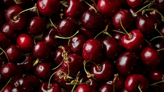 An overhead photograph of a large pile of dark-red cherries. 