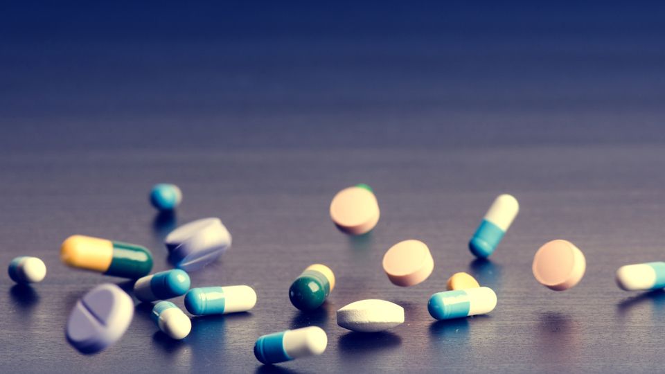 A selection of different pills and painkillers on a desk, which may be driving antibiotic resistance.