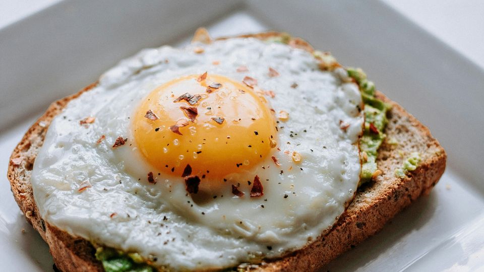 A fried egg on a piece of toast, green avocado visible between.