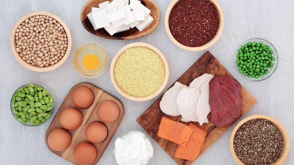 Assorted high-protein foods including meat, fish, eggs, tofu, legumes and grains on a table.