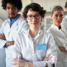 A group of life scientists in lab coats facing the camera, arms crossed with challenging looks on their faces. 